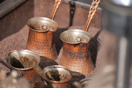 Copper coffee pots sit on fine sand in a bustling marketの写真素材