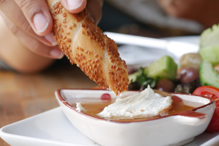 turkish simit bread being dipped into creamy sauceの写真素材