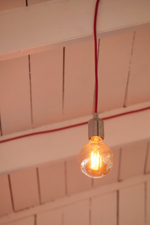 Hanging light bulb with warm glow against wooden ceilingの写真素材