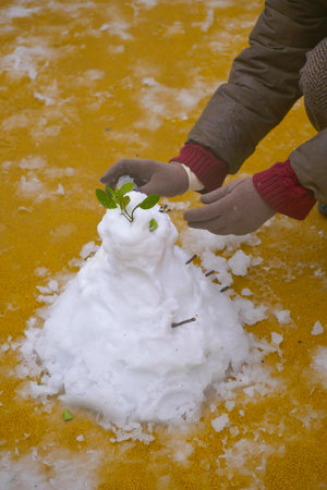 Building a snowman with green leaves on a vibrant yellow surfaceの写真素材