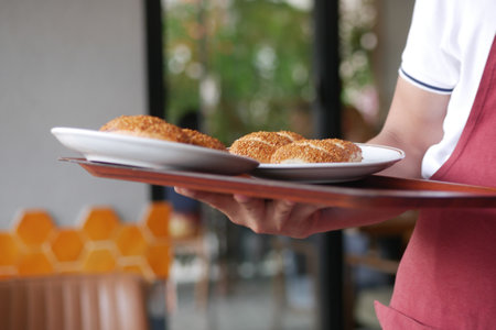 Waiter serves golden pastries on a wooden tray in a cozy cafeの写真素材