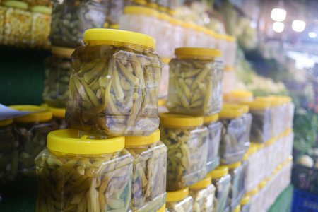 Jars of preserved vegetables at a vibrant market during daylight hours