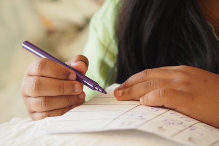 Child writing notes with a purple pen on a cozy surfaceの写真素材