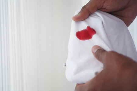 Red stain on white fabric being inspected closely by a handの写真素材