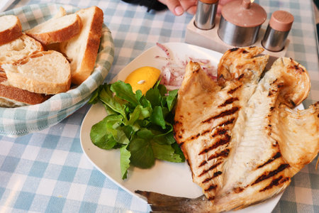 Delicious grilled fish served with fresh greens and breadの写真素材