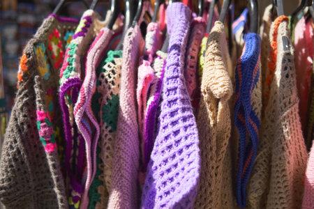 Colorful knitted garments displayed at a market stall in sunlightの写真素材