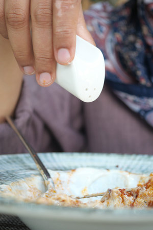 A hand sprinkles salt onto flavorful food at a casual dining setting