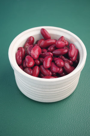Red kidney beans in a white bowl on a green surface