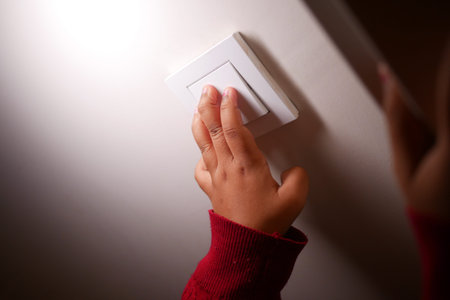 Child reaches for a light switch in a dimly lit room