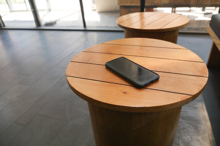 Phone resting on wooden table in modern lounge area.の写真素材