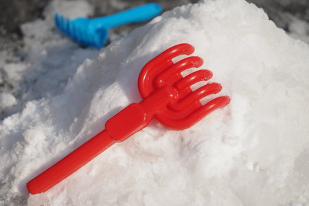 Colorful red plastic toy rake on a snowy surface during winterの写真素材