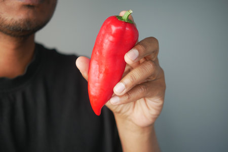 Man holding a red chili pepper indoors in a neutral settingの写真素材