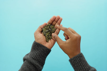 Hands holding green pumpkin seeds against a blue backgroundの写真素材