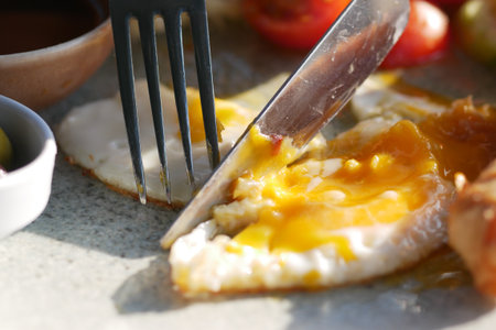 Perfectly cooked egg being cut with fork and knifeの写真素材