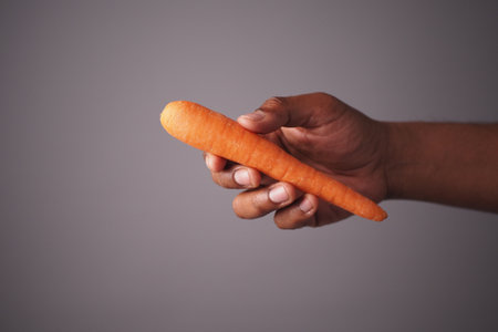 Hand holding a fresh carrot in a neutral backgroundの写真素材
