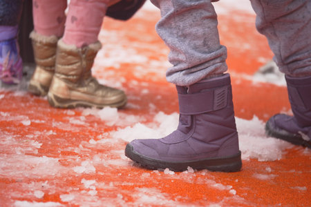 Children playing in snow with colorful winter boots in cityの写真素材