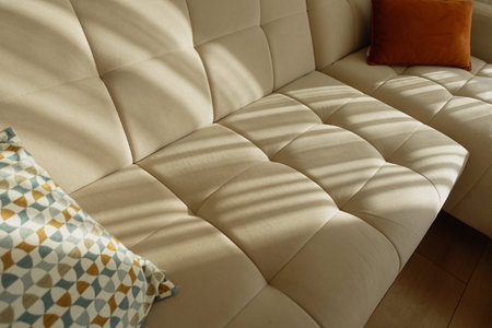 Comfortable beige sofa with decorative cushions in sunlight