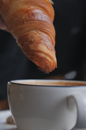 Croissant nearing cup of coffee in cozy cafe setting