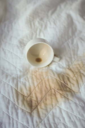 Coffee stain on a bedspread with empty mug nearby
