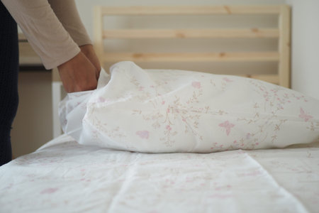 Preparing bed linens in a cozy bedroom settingの写真素材
