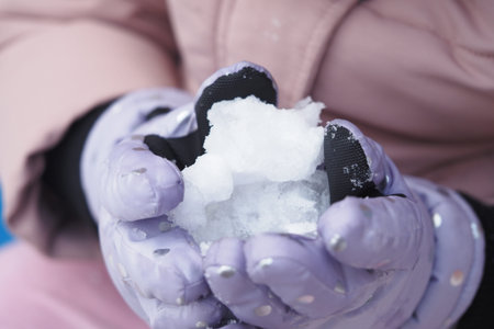 Child plays with snow in warm gloves on a winter dayの写真素材