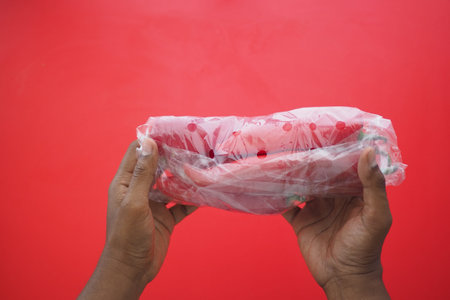 Hands Holding Wrapped capsicum Against a Bright Red Background