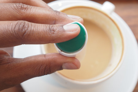 young man putting artificial sweetener into a cup of tea on table .