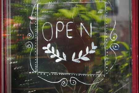 Open sign on cafe window surrounded by greenery