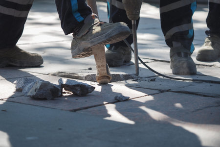 Construction workers use a jackhammer to break concrete while working.