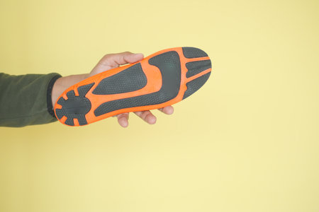 Hand with black and orange shoe sole on yellow backdropの写真素材