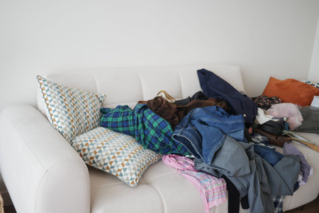 Cluttered couch with piles of clothes and cushionsの写真素材