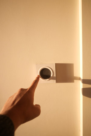 Hand adjusting thermostat on a warm wall in the afternoon