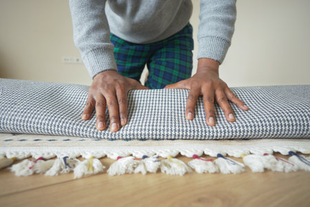 Person rolling up a checkered rug on a wooden floorの写真素材