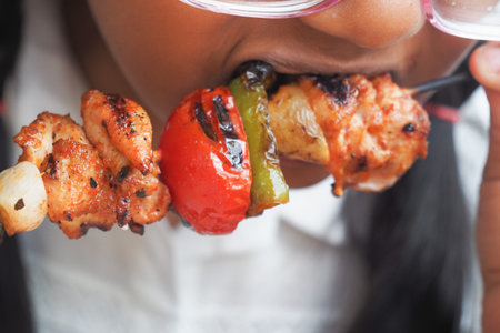 little Girl Enjoying a delicious grilled kebab at a summer barbecueの写真素材