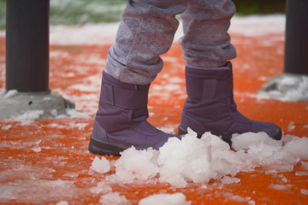 Child playing in snow with purple boots during winterの写真素材