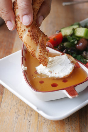 A hand dips bread into a bowl of honey topped with cheeseの写真素材