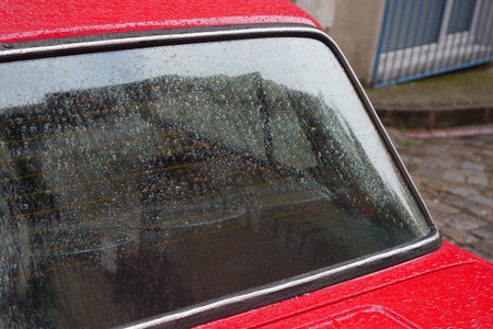 Rain-soaked red car parked on cobblestone street