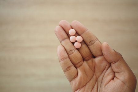 Hand holding four pink pills on a wooden surfaceの写真素材