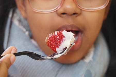 Young girl enjoying a strawberry dessert with creamの写真素材