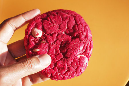 Bright red cookie held against a vibrant orange backgroundの写真素材