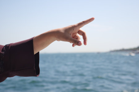 Hand pointing toward the horizon over tranquil waterの写真素材