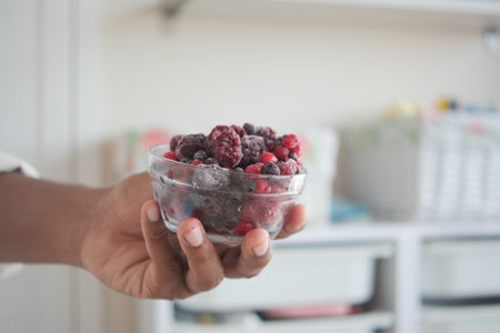 Holding a bowl of mixed frozen berries in a kitchenの写真素材