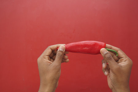 Hands holding a red chili pepper against a red backgroundの写真素材