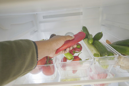 Fresh vegetables in refrigerator with hand selecting peppersの写真素材