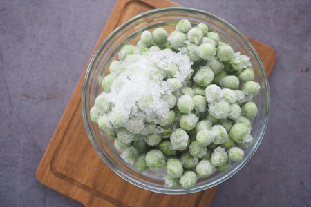 Frozen green peas in a glass bowl on a wooden cutting boardの写真素材