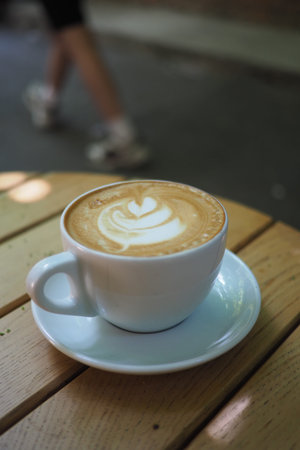 Coffee cup with latte art on wooden table outdoors