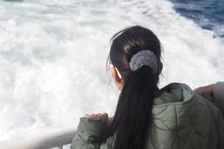 Girl looks out at ocean waves from a boat deckの写真素材