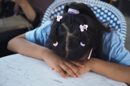 Child resting with head down on a table in a cafeの写真素材