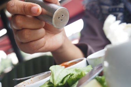 Hand adding seasoning to fresh salad in outdoor restaurantの写真素材