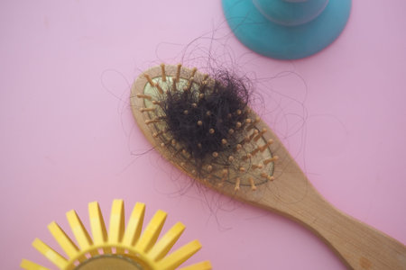 A wooden hairbrush with loose hair on a pink background .